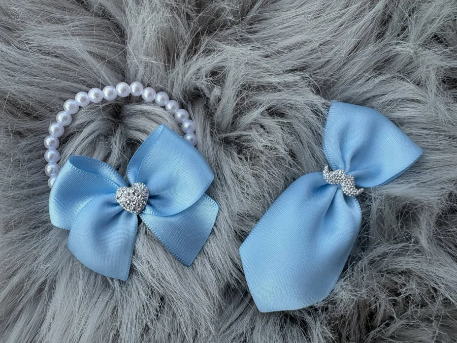 Biserna narukvica s plavom mašnicom i srebrnim srcem pored plavog revera sa srebrnim brkovima stoje na čupavom sivom tepihu.