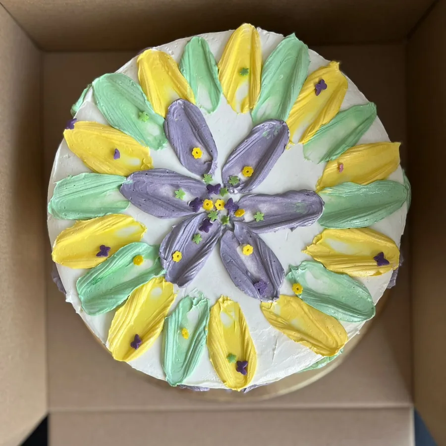 Bijela torta u kutiji s žutim, zelenim i ljubičastim pastelnim bojama.