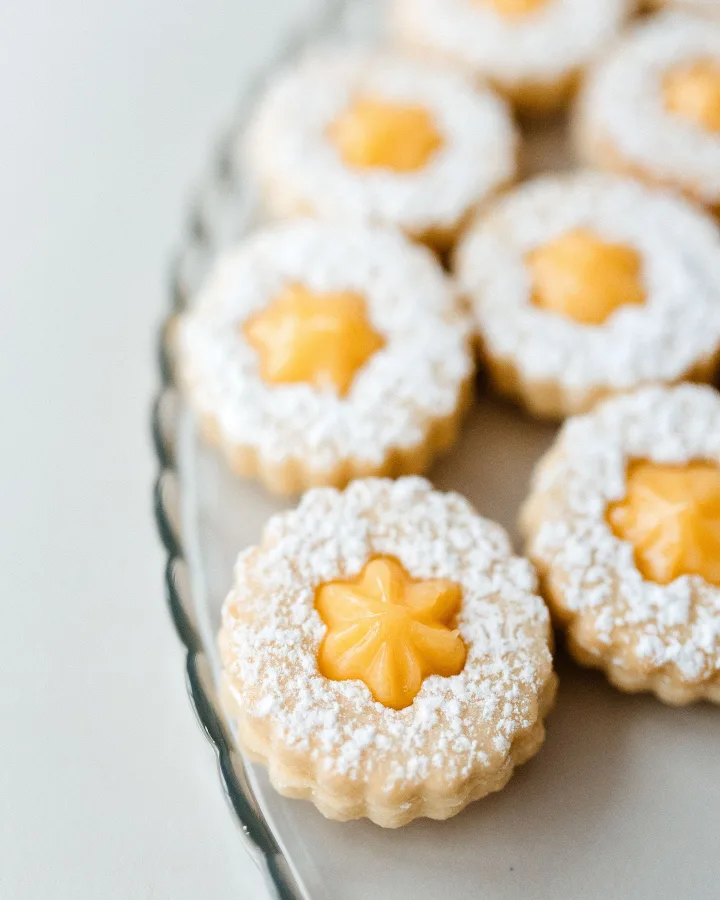 Slika izbliza suhi kolači linzeri punjeni kremom i prosuti šećerom u prahu.