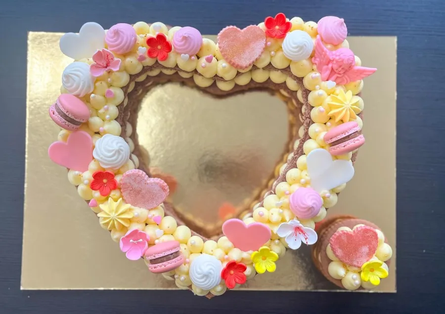 Torta u obliku srca s žutom kremom, rozim čokoladicama i makaronima.