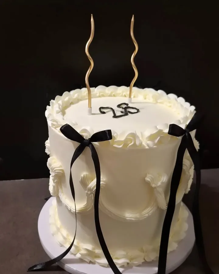 Bijela torta za rođendan s crnim nejestivim mašnicama i natpisom od čokolade "28".