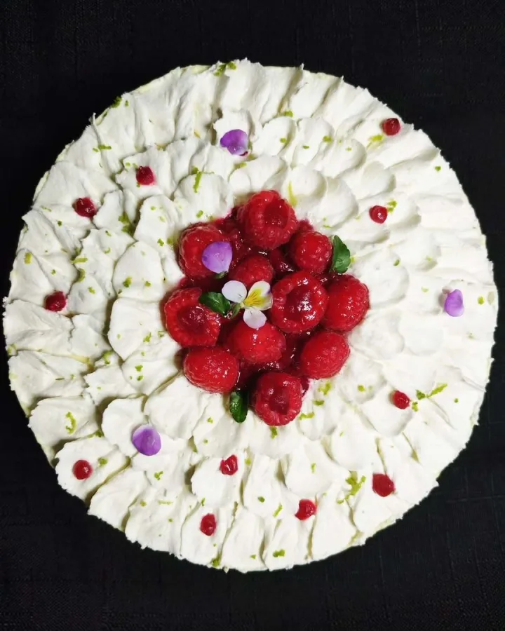 Vrh torte s bijelim laticama i malinama u sredini.