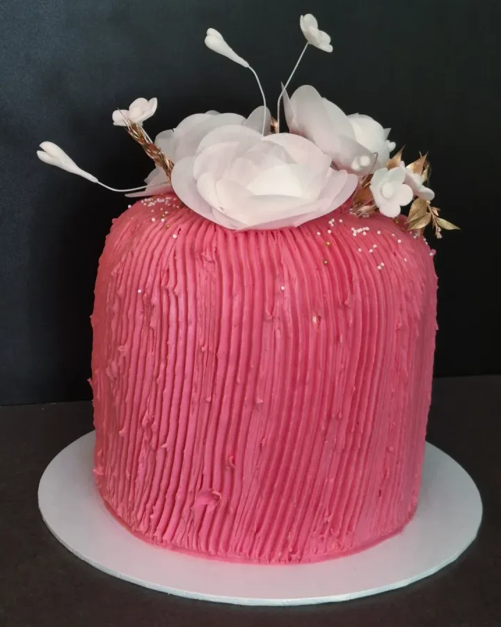 Ružičasta okrugla torta s udubljenim linijama i bijelim cvijećem na vrhu.