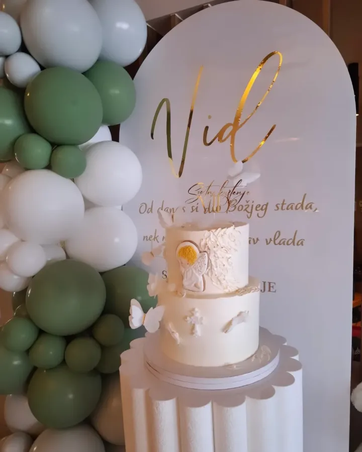 Bijela torta s anđelom i leptirima za krštenje dječaka Vida na stalku pokraj dekoracije s natpisom "Vid".