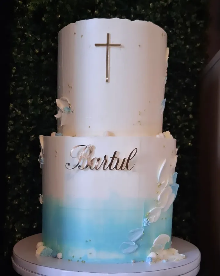 Torta za krštenje s natpisom "Bartul" na dva kata. Prvi kat počinje s plavom bojom koja prelazi u bijelu, a drugi je posve bijel.
