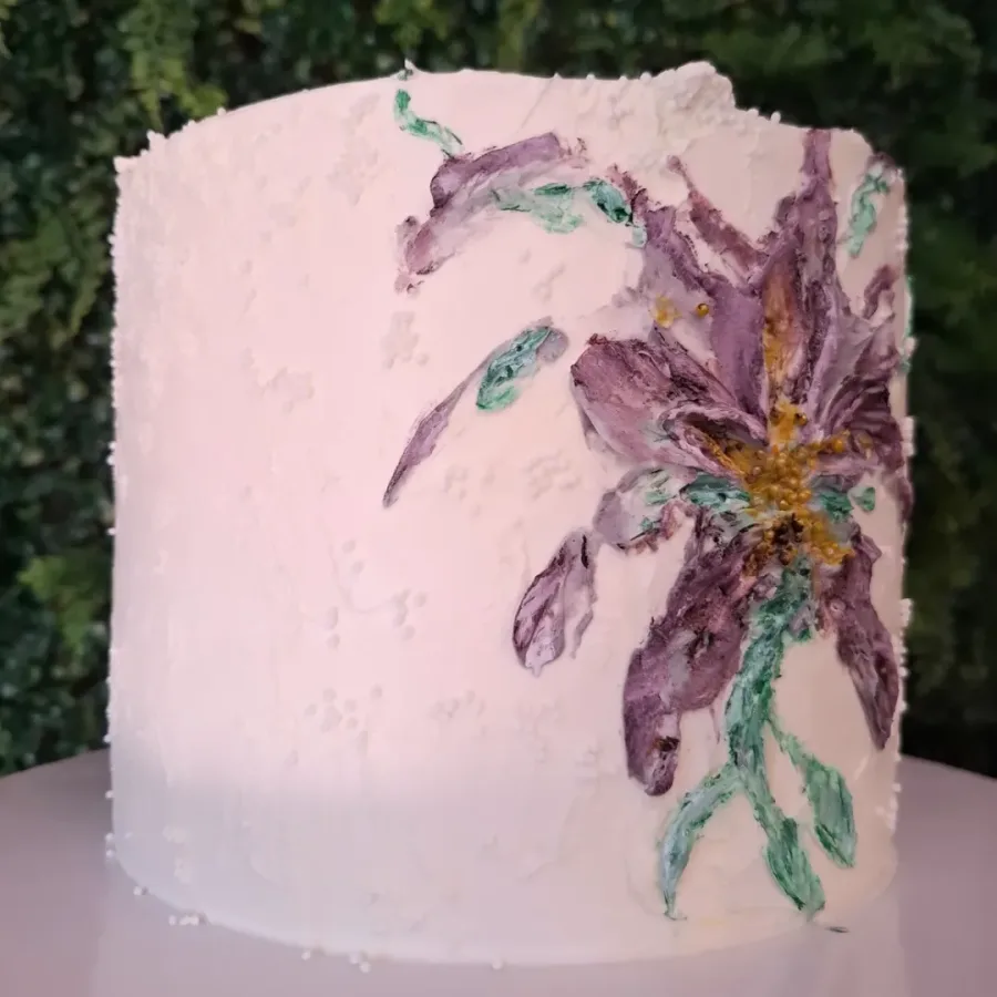 Bijela torta s ljubičastim cvijetom, žutim tučkom i zelenim lišćem od kreme.