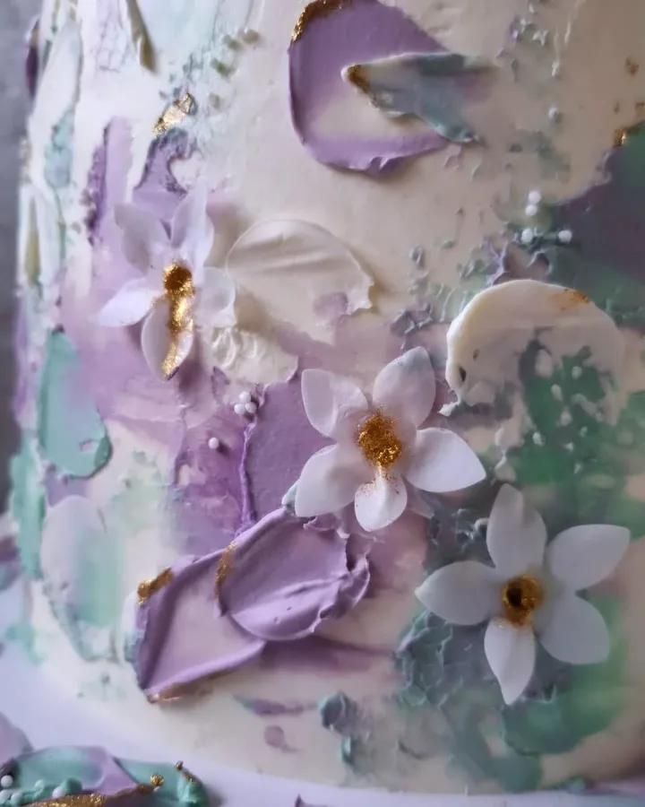 Ljubičaste i zelene latice od kreme na bijeloj torti s bijelim cvijećem.