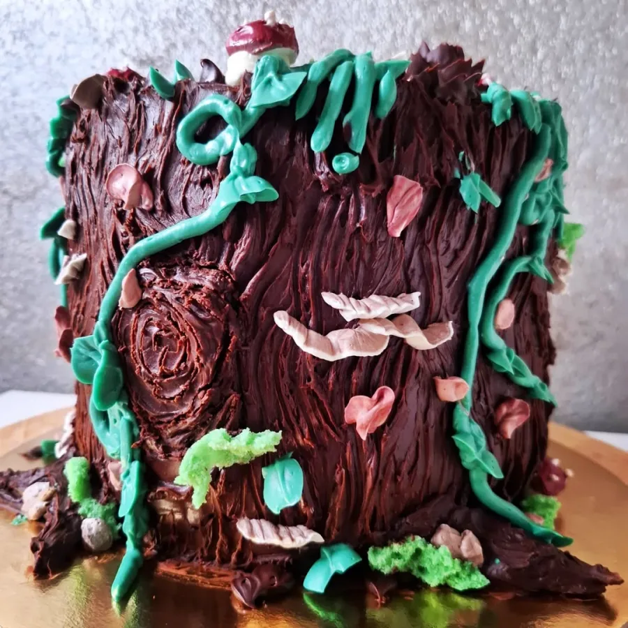 Smeđa torta ukrašena kao deblo od stabla s travama i mahovinom.