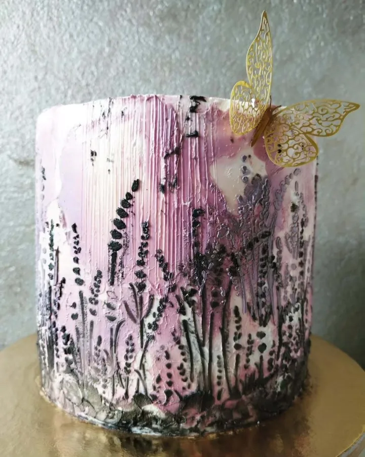 Bijela torta s ružičastim mrljama i crnim cvijećem te zlatnim leptirom kao ukras.