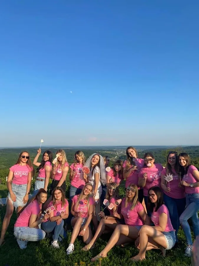 Djevojka i buduća mladenka poziraju za fotografiju za vrijeme djevojačke u vili za vjenčanja. Djevojke nose ružičaste majice, a buduća mladenka je u bijelom.