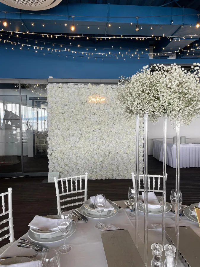 Zid s bijelim ružama i neonskim natpisom 'Cheers to love', u sali za vjenčanje.