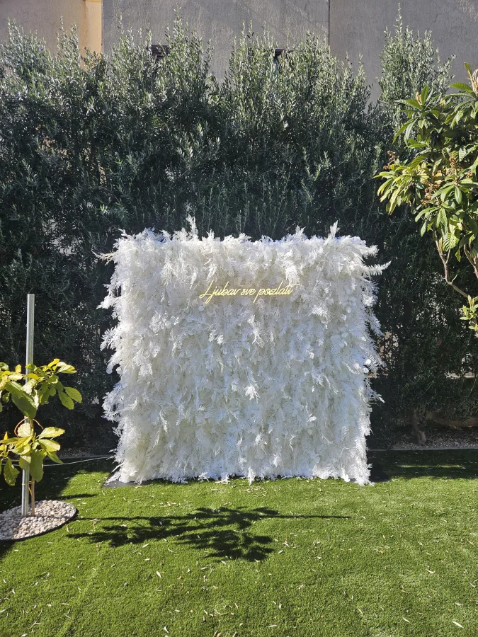 Bijeli zid od perja s neonskim natpisom 'ljubav sve pozlati', idealan za fotografiranje na vjenčanju.