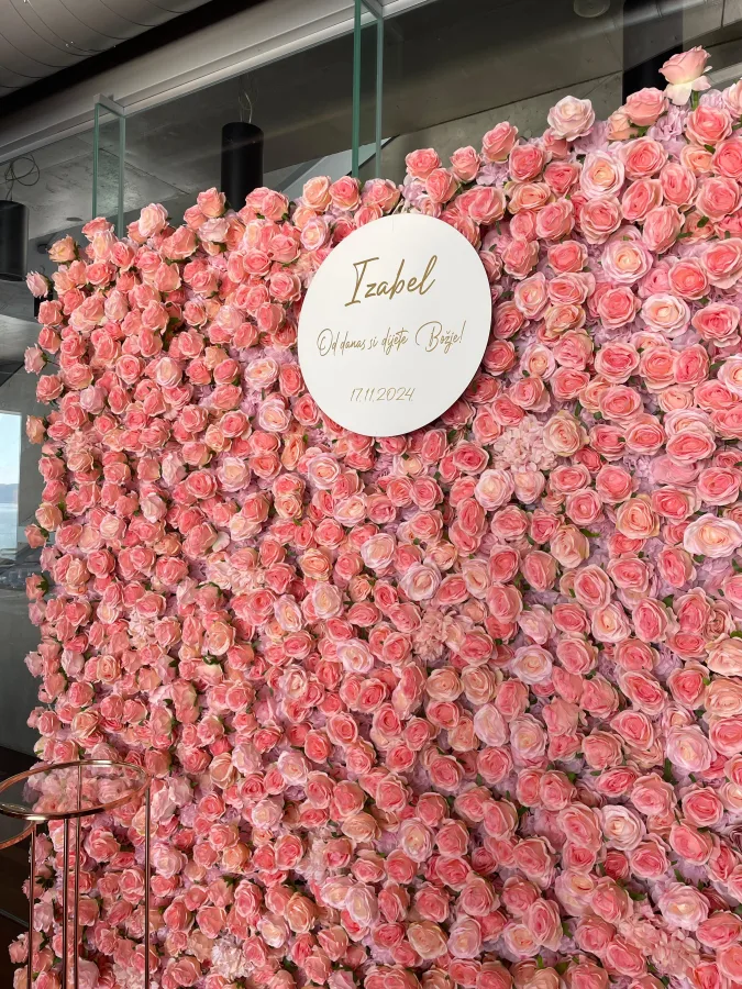 Zid s ružičastim ružama i natpisom 'Izabel, od danas si dijete Božje!', idealan za fotografiranje na krštenju.